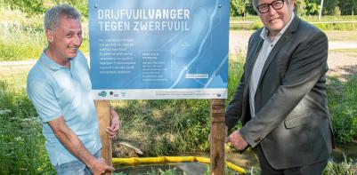 Gedeputeerde Bart Nevens en schepen Gary Peeters plaatsen het infobord aan de drijfvuilvanger in de Dormaalbeek in Landen